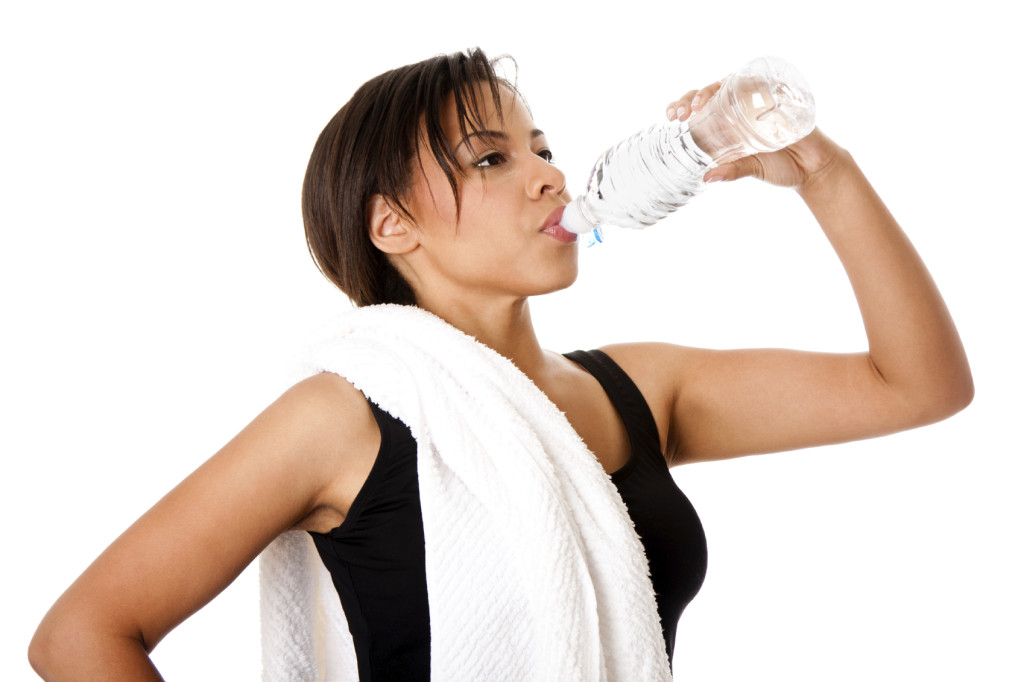 Beautiful attractive young sweaty woman drinking water after exercise workout, rehydrating thirst quenching, isolated.